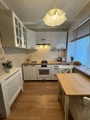 a kitchen with white cabinets and a table and a chandelier at Jaukus apartamentas Birzu centre in Biržai
