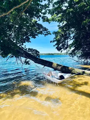 a person laying in a hammock on a lake at Sodyba Po klevu in Molėtai