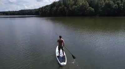 a man is rowing a paddle boat on a lake at Pasakų namelis dviems su vaizdu į ežerą in Esperanza