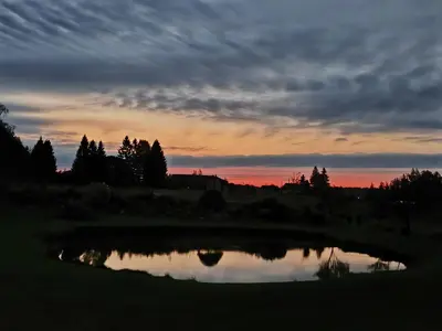 a sunset over a pond in a field at Užmiesčio trobelė in Mackėnai