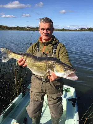 a man standing on a boat holding a large fish at Marių Kalvos in Palėvenėlė