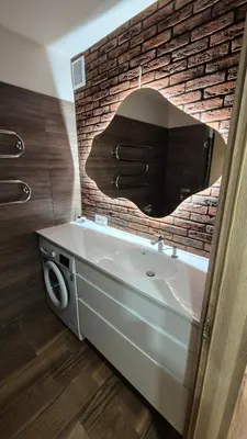 a bathroom with a white sink and a brick wall at Savannah Ateities Apartamentai in Panevėžys