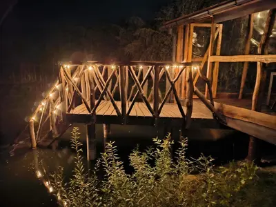 a wooden bridge with lights on the water at night at Egliškių Oazė Sodyba su pirtimi kubilu- privatumas garantuotas in Vilnius