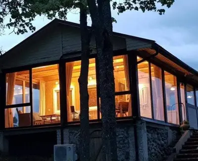 a house with large glass windows and a tree at Svedaso Lake House with Sauna in Svėdasai