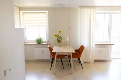 a dining room with a table and chairs and two windows at Močiutės apartamentai in Anykščiai
