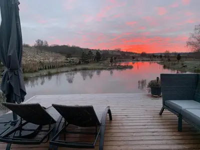 a wooden deck with two chairs and a lake at Aurora Resort in Stasiūnai