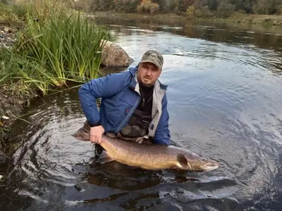a man holding a large fish in the water at Senosios Gegužinės ūkis in Gegužinė
