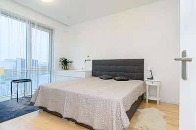 a white bedroom with a bed and a large window at Cute apartment Konstitucijos ave in Vilnius