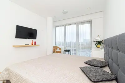 a white bedroom with a bed and a flat screen tv at Cute apartment Konstitucijos ave in Vilnius