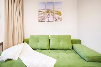 a living room with a green couch in a room at Stylish white salad studio near the city center in Vilnius