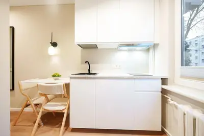 a white kitchen with a sink and a table at Stylish white salad studio near the city center in Vilnius