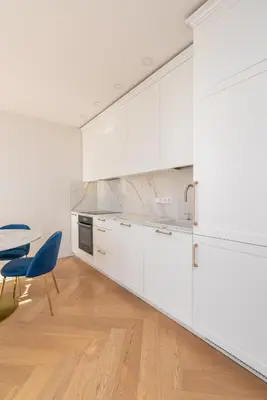 a kitchen with white cabinets and a table and a blue chair at The Zen Den Apartment in Uzupis in Vilnius