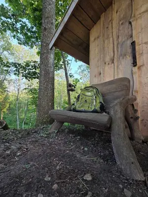 a green backpack sitting on a bench in the woods at Terra Gratia - namukas Natūralistas in Nemeikšiai