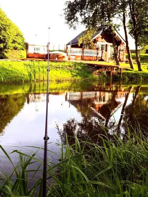 a pond with a house and a bridge in the background at Sodyba Barracuda in Kupščiai