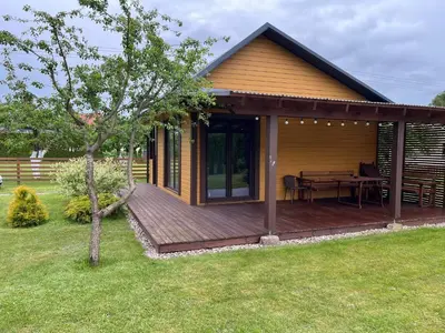 a house with a wooden deck with a table at Namelis Saulės gatvėje prie Siesarties ežero in Molėtai