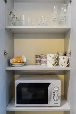 a microwave on a shelf with cups and plates at Greimo Apartments in Šiauliai