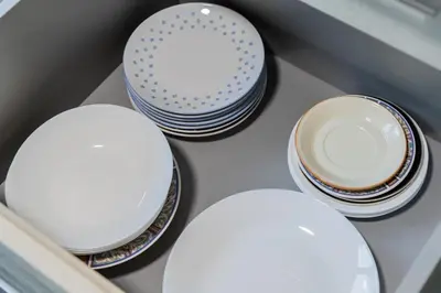 four white plates and bowls sitting on a shelf at Greimo Apartments in Šiauliai