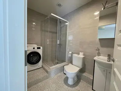 a bathroom with a toilet and a shower and a washing machine at PERLOS apartamentai 2a in Birštonas