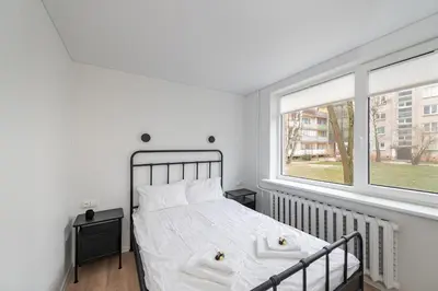 a bedroom with a bed with white sheets and two windows at Apartment Dandelion by Polo Apartments in Kaunas