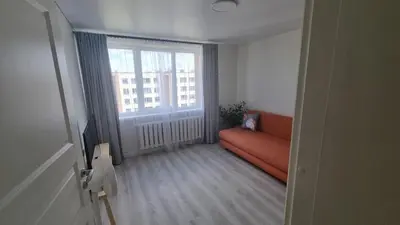 a living room with an orange couch and a large window at Tiny cozy apartment 'Unihus' in Varėna
