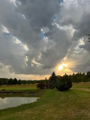 a cloudy sky over a field with a pond at Sekioniu Ranch - Cosy Wooden Cabins in Lithuania in Sekionys
