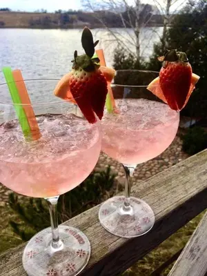 two glasses with strawberries in them sitting on a wooden rail at Apartamentai prie ežero in Vilnius