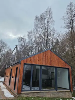a wooden house with glass windows in a field at Pasienio Krantas in Velūnai