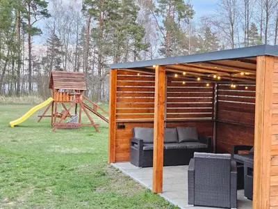 a wooden gazebo with a bench and a playground at Pasienio Krantas in Velūnai
