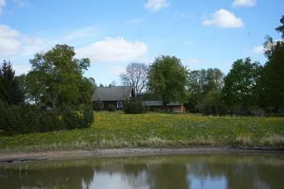 a house in a field next to a body of water at Molinis ir Medinis in Ažuluokesa