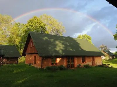 a rainbow over a wooden house with a green roof at Molinis ir Medinis in Ažuluokesa