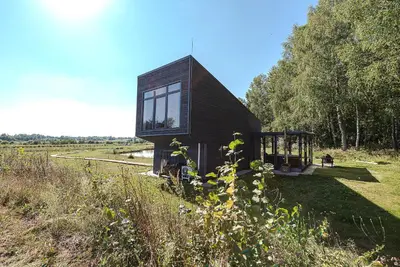 a small house with glass windows on a field at Namelis Ramybėlė in Siauliškiai