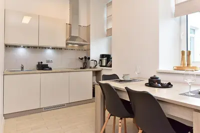 a kitchen with white cabinets and a wooden table with chairs at Apartamentai DU in Druskininkai