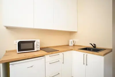 a kitchen with white cabinets and a microwave and a sink at Compact and Comfy Apartment on the Greenhill in Kaunas