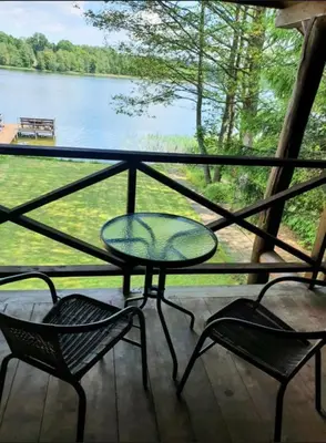 a table and chairs on a porch with a view of a lake at Atostogų namelis ant ežero kranto in Juočionys