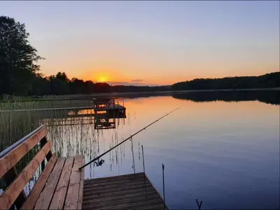 a sunset on a lake with a dock and a boat at Atostogų namelis ant ežero kranto in Juočionys
