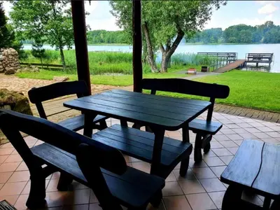 a picnic table with benches and a view of a lake at Atostogų namelis ant ežero kranto in Juočionys