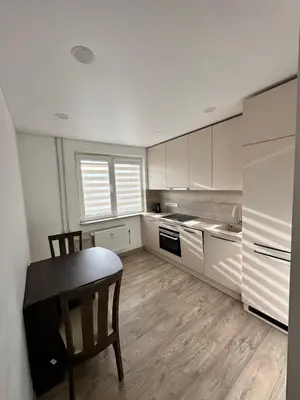 a kitchen with white cabinets and a table and a chair at Lauros Apartamentai in Kupiškis