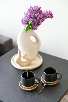 two cups of coffee on a table with a vase of lilacs at GOOD LOCATION studio near the old town - station - airport - self check in in Vilnius