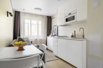 a white kitchen with a table with a bowl of fruit on it at GOOD LOCATION studio near the old town - station - airport - self check in in Vilnius