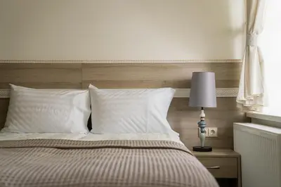 a bed with white pillows and a table with a lamp at Birštono Banginukas poilsio namai in Birštonas