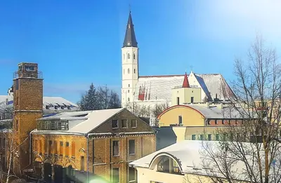 a large church with a steeple and a building with snow at Central Apartment with Fireplace & Cathedral View in Šiauliai