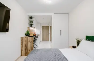 a white bedroom with a bed and a kitchen at Green Apartment in Vilnius