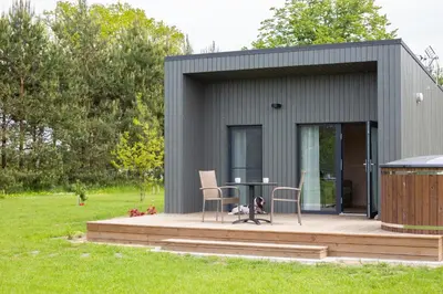 a tiny house with a deck and a table and chairs at Rasota Pieva Dewy Meadow