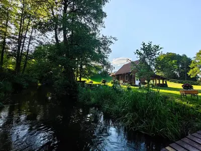 a river with a house in the background and a building at Sodyba LAIMĖS SLĖNIS in Kapčiamiestis