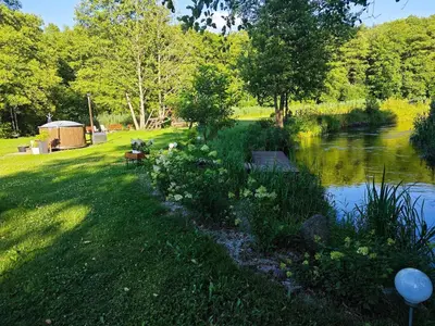 a grassy yard with a river and a gazebo at Sodyba LAIMĖS SLĖNIS in Kapčiamiestis