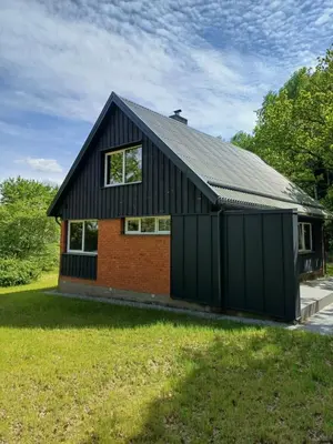a house with a black roof and a grass yard at Valva vila in Luokesos Sen