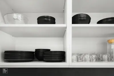 a white cabinet filled with black plates and bowls at Comfortable 2 BD Apartment by Domvia in Kaunas