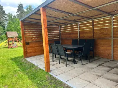 a wooden pergola with a table and chairs on a patio at Pasienio krantas in Velūnai