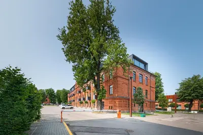 a red brick building with a tree in front of it at Shanti barracks apartment #3 by Polo Apartments in Kaunas
