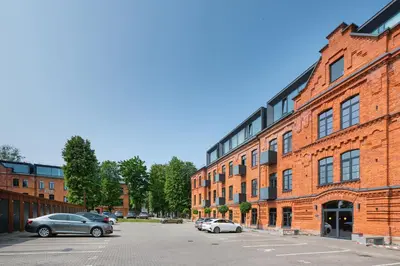 a red brick building with cars parked in a parking lot at Shanti barracks apartment #3 by Polo Apartments in Kaunas